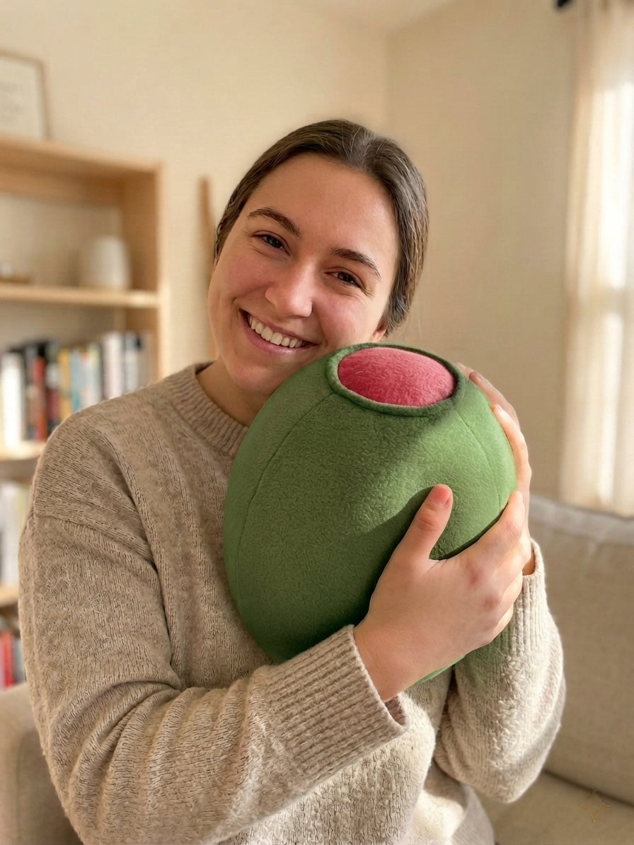 Smiling woman in a cozy sweater hugging a martini olive plush pillow, a cute stocking stuffer for a girlfriend