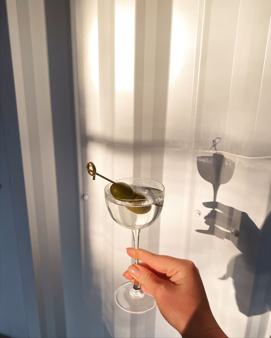 Hand holding a martini glass garnished with green olives on a pick