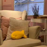 Goldfish cracker plush resting on a cozy armchair with pink cushions