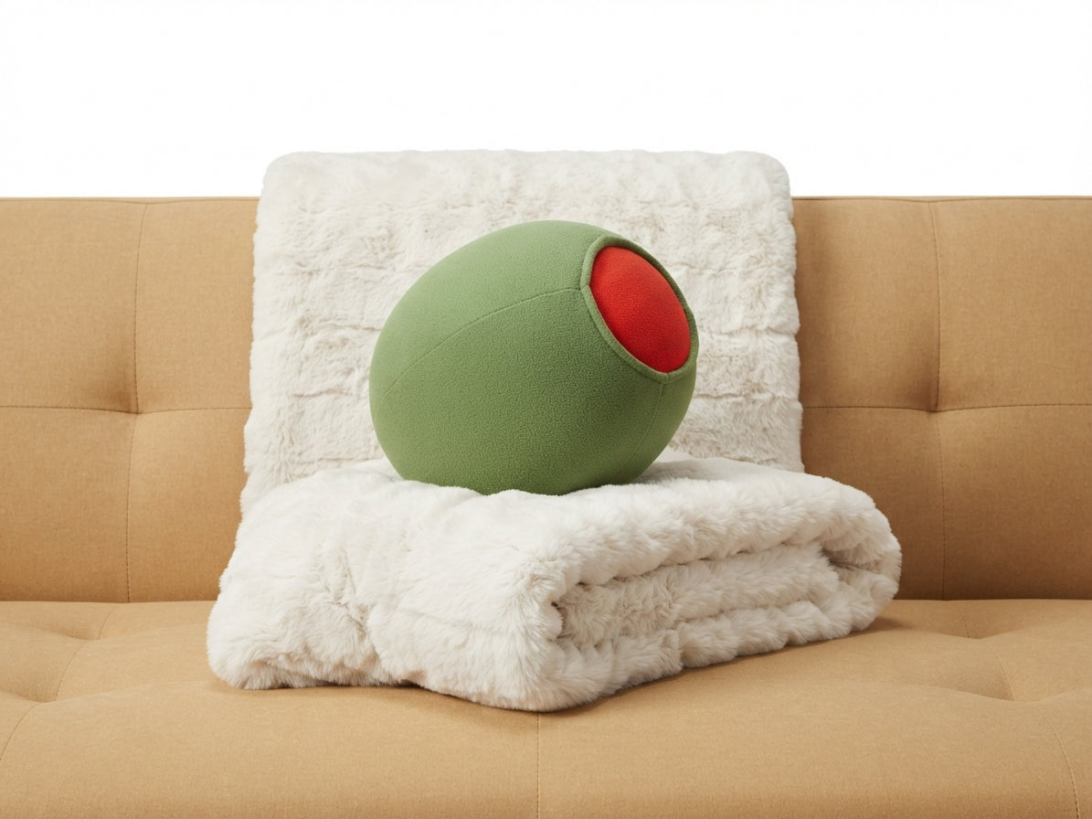 Martini olive plush pillow resting on a white faux-fur throw on a tan sofa