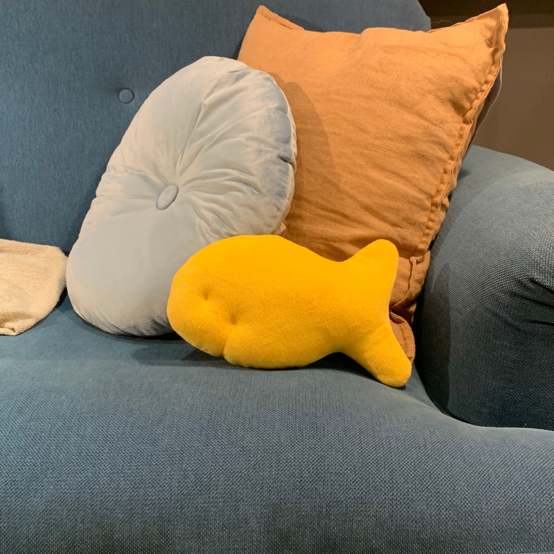 Cheddar fish cracker plush used as a small pillow on a sofa