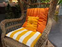 Cheese cracker plush pillow on a wicker patio chair with orange cushions