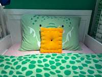 Cheese cracker plush pillow on a child's bed with green dinosaur bedding