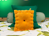 Cheese cracker plush pillow propped against a green cushion on a bed